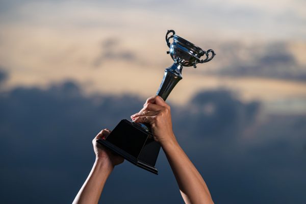 a man holding up a trophy cup on against cloudy twilight sky background, The winner and successful concept